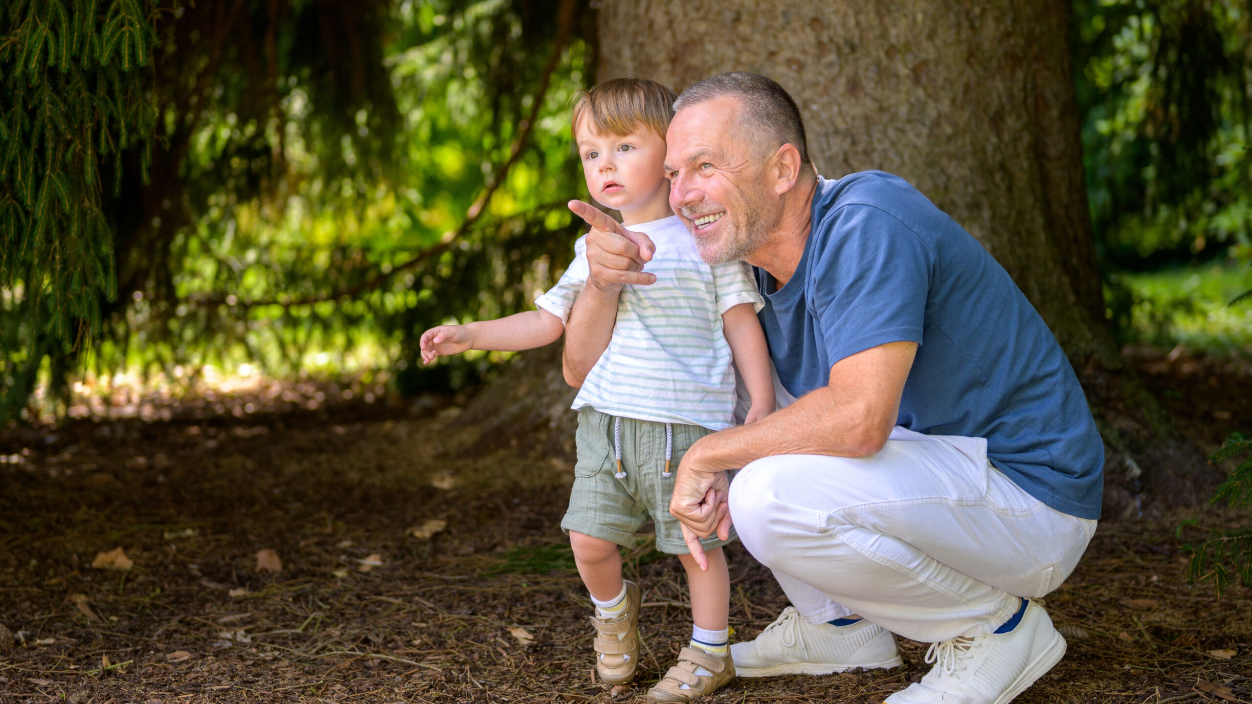 smiling,grandfather,crouching,next,to,his,curious,toddler,grandson,in
