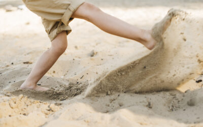Happy Kids Boutique sfeerbeeld van een kind dat op het strand met blote voeten door het zand rent en zand wegschopt, passend bij buiten spelen en bewust genieten van duurzaamheid.