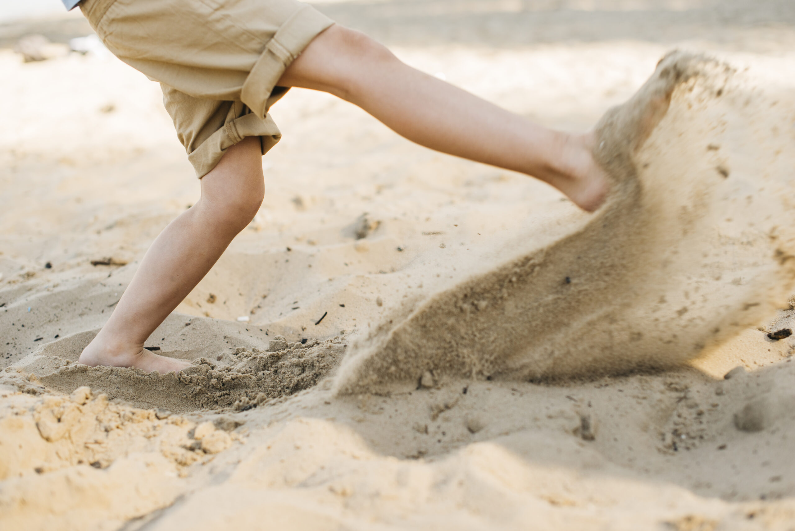 Happy Kids Boutique sfeerbeeld van een kind dat op het strand met blote voeten door het zand rent en zand wegschopt, passend bij buiten spelen en bewust genieten van duurzaamheid.