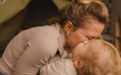 Happy Kids Boutique beeld van een ouder die liefdevol een kind kust terwijl ze samen op de grond zitten bij een speeltent, een warm moment van quality time en verbondenheid met aandacht voor duurzaamheid en geborgenheid