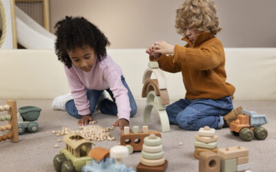 Twee kinderen spelen op een zachte vloer met houten speelgoed en stapelblokken in rustige natuurlijke kleuren, een sfeervol beeld dat past bij Happy Kids Boutique waar babykleding en babybenodigdheden samenkomen met aandacht voor spel, comfort en duurzaamheid. Afbeelding designes by Freepik.