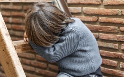 Happy Kids Boutique kind zit buiten op een houten trap met hoofd op de armen en oogt boos en gefrustreerd tegen een bakstenen muur, moment van emotie met aandacht voor duurzaamheid