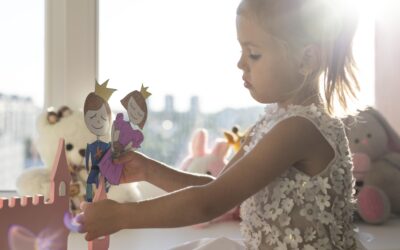 Jong meisje speelt bij het raam met houten poppetjes en speelgoed in een lichte kinderkamer, gekleed in zachte babykleding, een sfeervol beeld dat past bij Happy Kids Boutique waar babykleding en babybenodigdheden samenkomen met aandacht voor comfort en duurzaamheid. Afbeelding designed by Freepik.