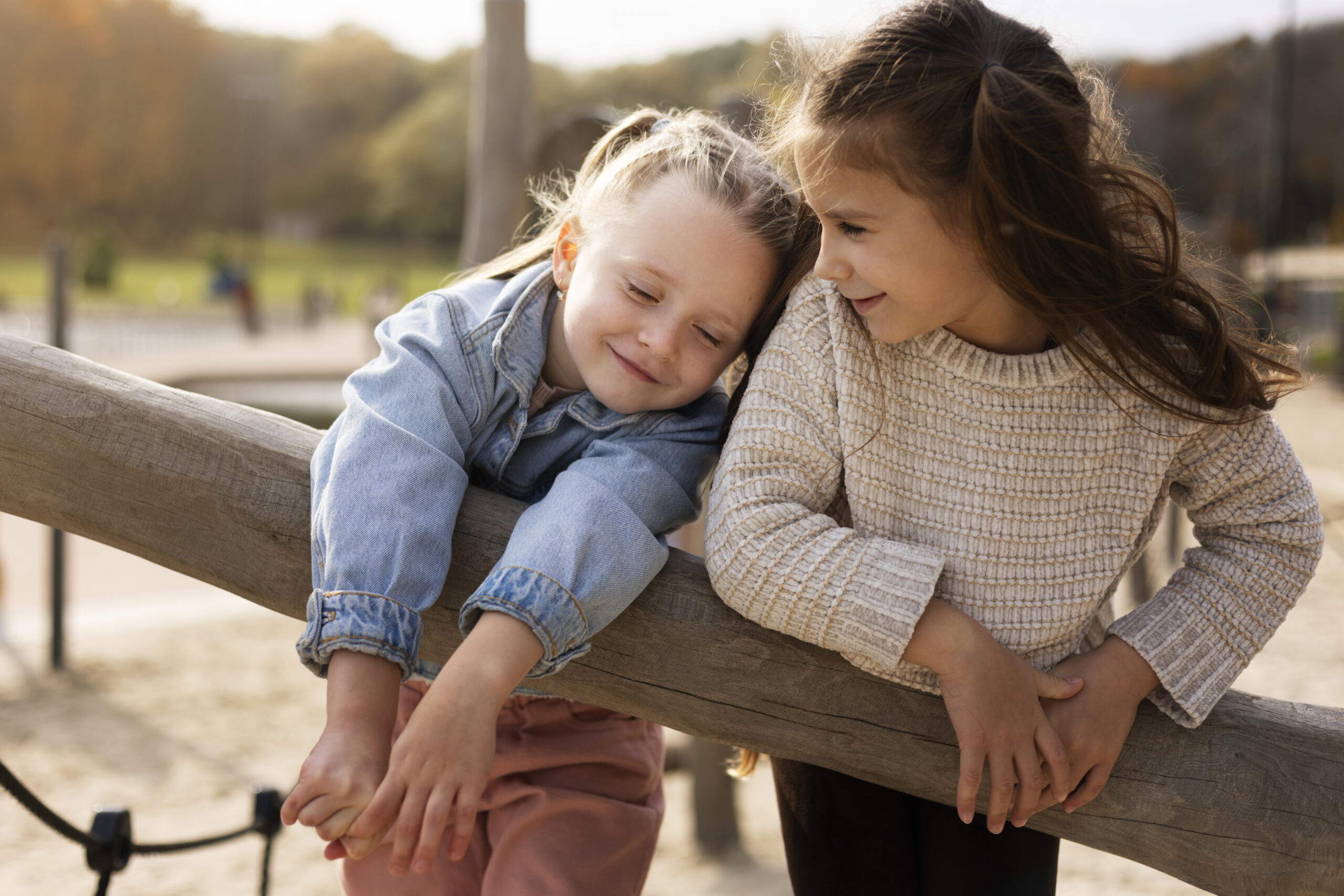 Blogfoto de eerste vriendschappen Twee kinderen leunen samen op een houten speeltoestel en lachen terwijl ze dicht tegen elkaar aan zitten in een buitenomgeving. Het moment straalt warmte en vriendschap uit tussen de kinderen tijdens het spelen. Deze sfeerafbeelding van Happy Kids Boutique benadrukt verbinding, samenzijn en een bewuste levensstijl met aandacht voor duurzaamheid.