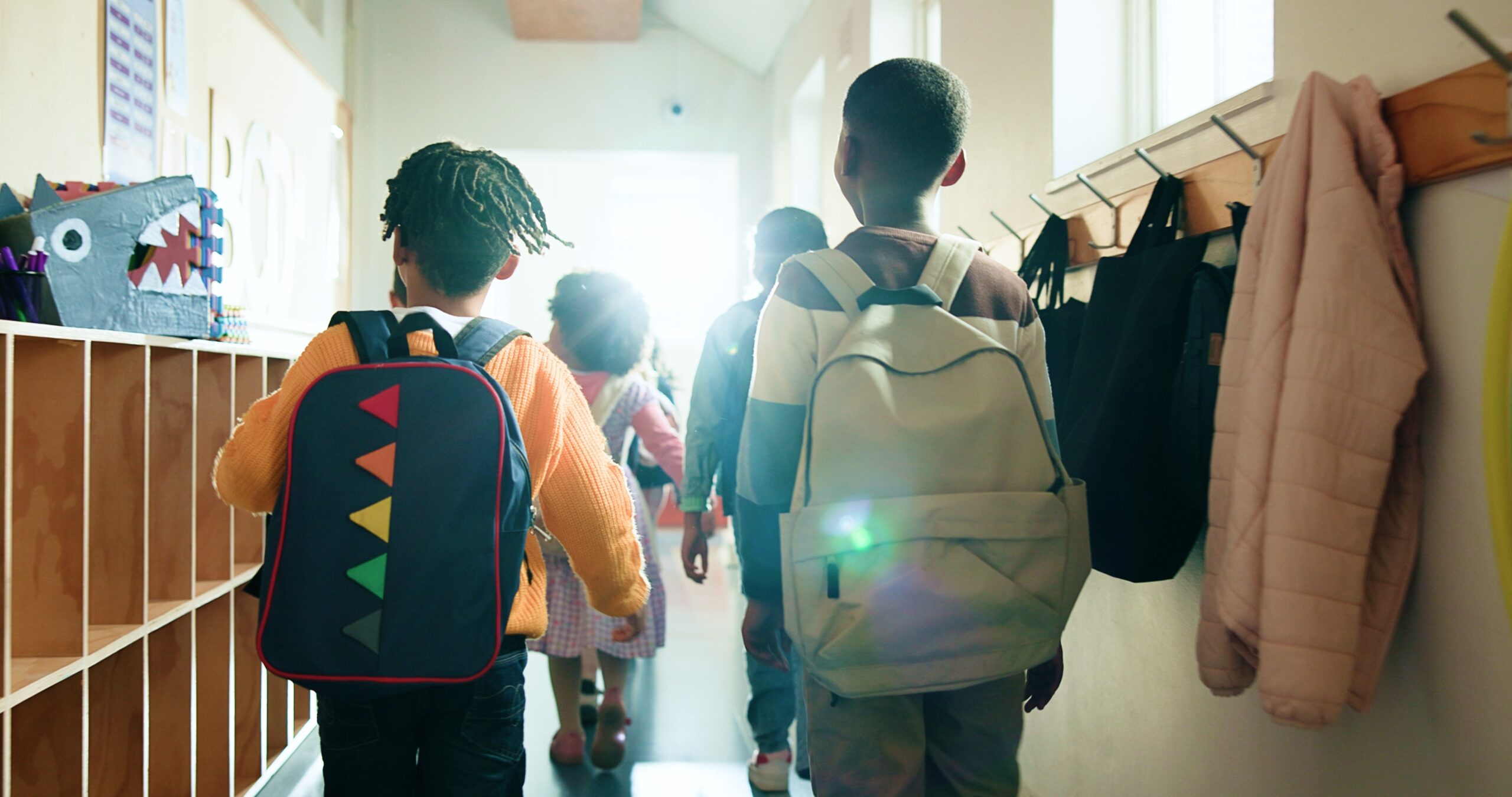 Kinderen lopen met rugzakken door de gang van een basisschool richting het klaslokaal, een dagelijks schoolmoment dat past bij Happy Kids Boutique waar babykleding en babybenodigdheden bijdragen aan comfort, ontwikkeling en duurzaamheid.