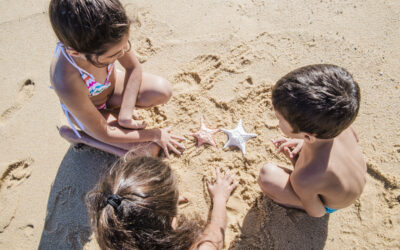 Happy Kids Boutique strand kinderen spelen spelletjes in het zand waarbij drie kinderen samen schelpen en vormen maken op het strand in de zon met aandacht voor duurzaamheid