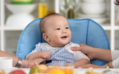 Happy Kids Boutique eten moment met kind in kinderstoel dat blij aan tafel zit tijdens het ontbijt met fruit en brood, warm gezinsmoment in huiselijke sfeer