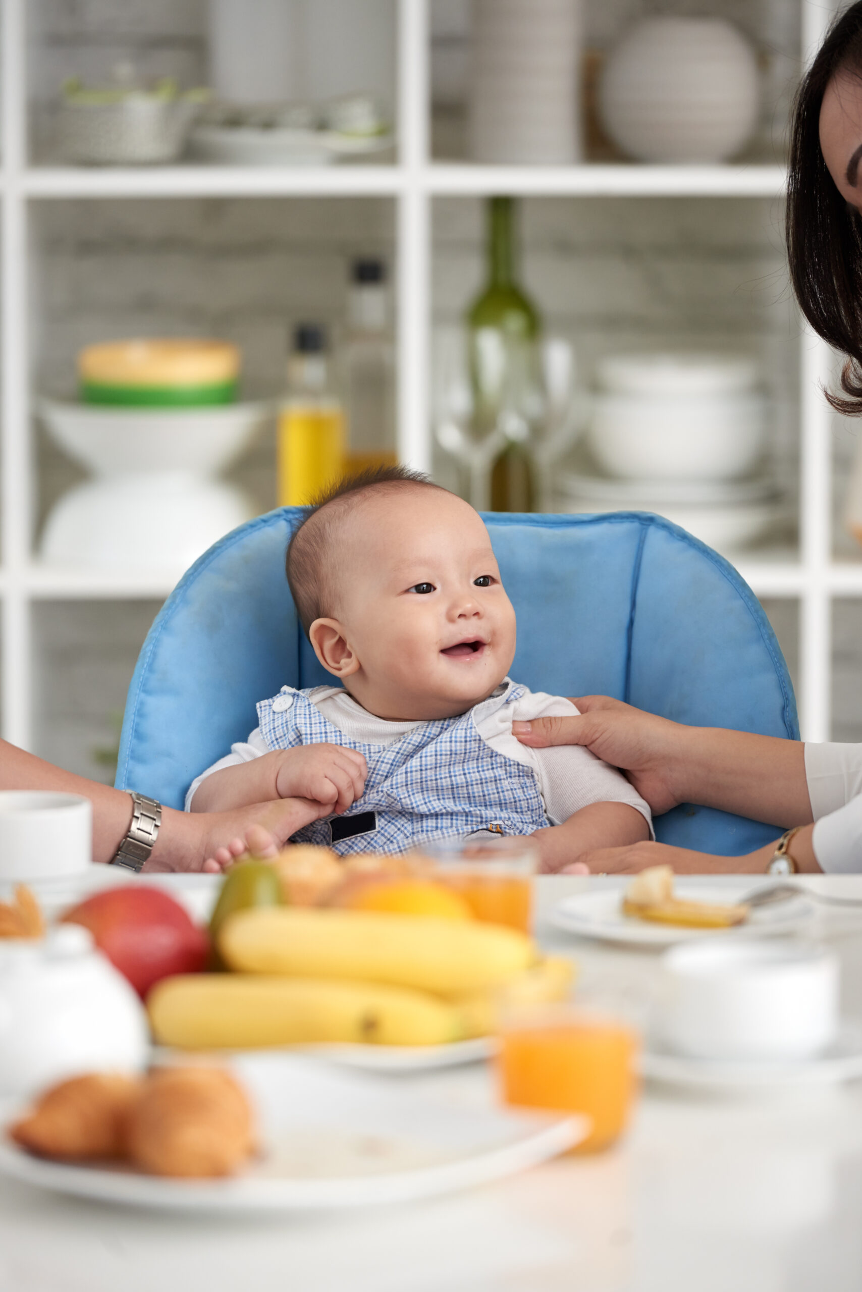 Happy Kids Boutique eten moment met kind in kinderstoel dat blij aan tafel zit tijdens het ontbijt met fruit en brood, warm gezinsmoment in huiselijke sfeer
