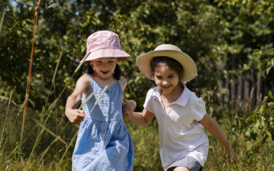 Happy Kids Boutique afbeelding van twee kinderen die samen spelen en rennen door het gras in de natuur, hand in hand en lachend, met ruimte voor vrij spel en geen oordeel