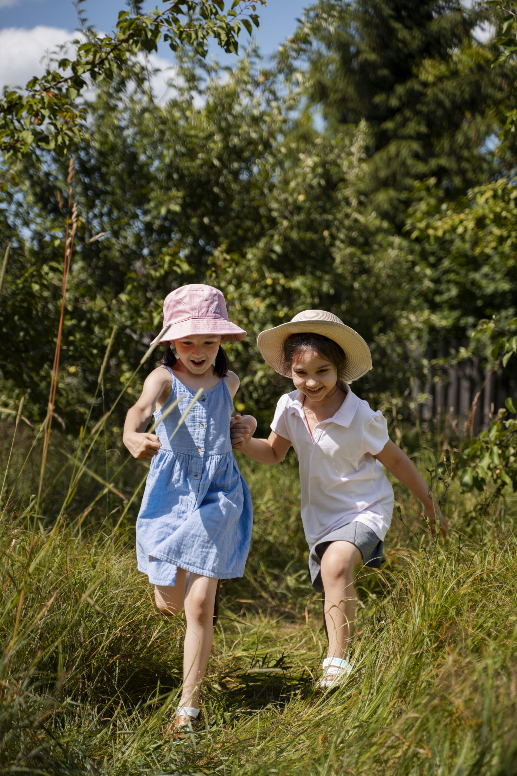 Happy Kids Boutique afbeelding van twee kinderen die samen spelen en rennen door het gras in de natuur, hand in hand en lachend, met ruimte voor vrij spel en geen oordeel