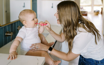 Happy Kids Boutique afbeelding van een moeder die een baby helpt met tandenpoetsen met een kleine tandenborstel van Dr. Brown's, waarbij de baby op het aanrecht zit en speels kennismaakt met mondverzorging