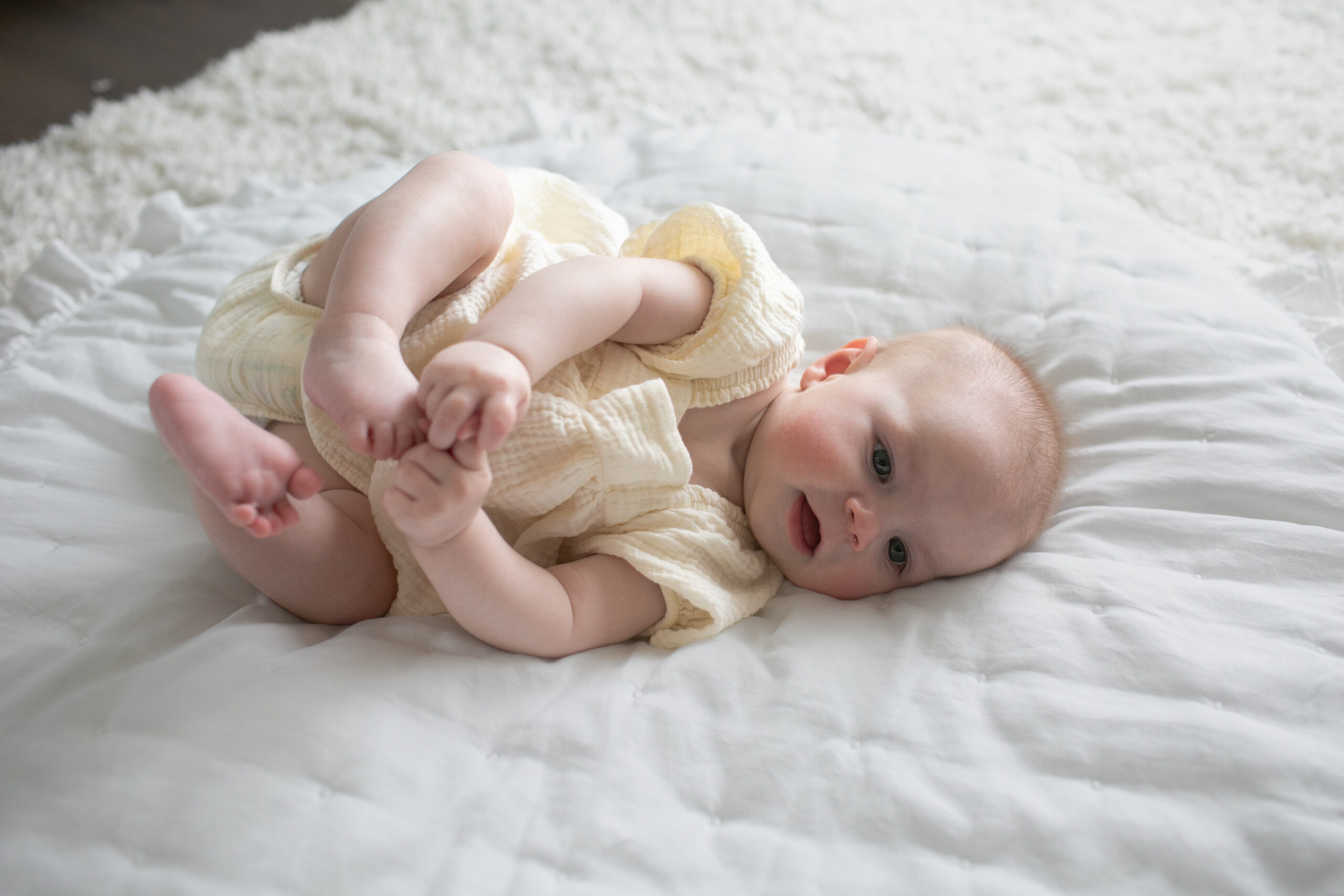 Happy Kids Boutique baby ligt op een zacht bed en speelt met zijn voetjes, vrolijk en ontspannen moment dat past bij inspiratie rondom babynamen