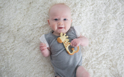 Happy Kids Boutique afbeelding van een baby die op een zachte ondergrond ligt en een bijtring vasthoudt, geschikt bij doorkomende tandjes, waarbij de baby rustig speelt met een Dr. Brown's bijtring