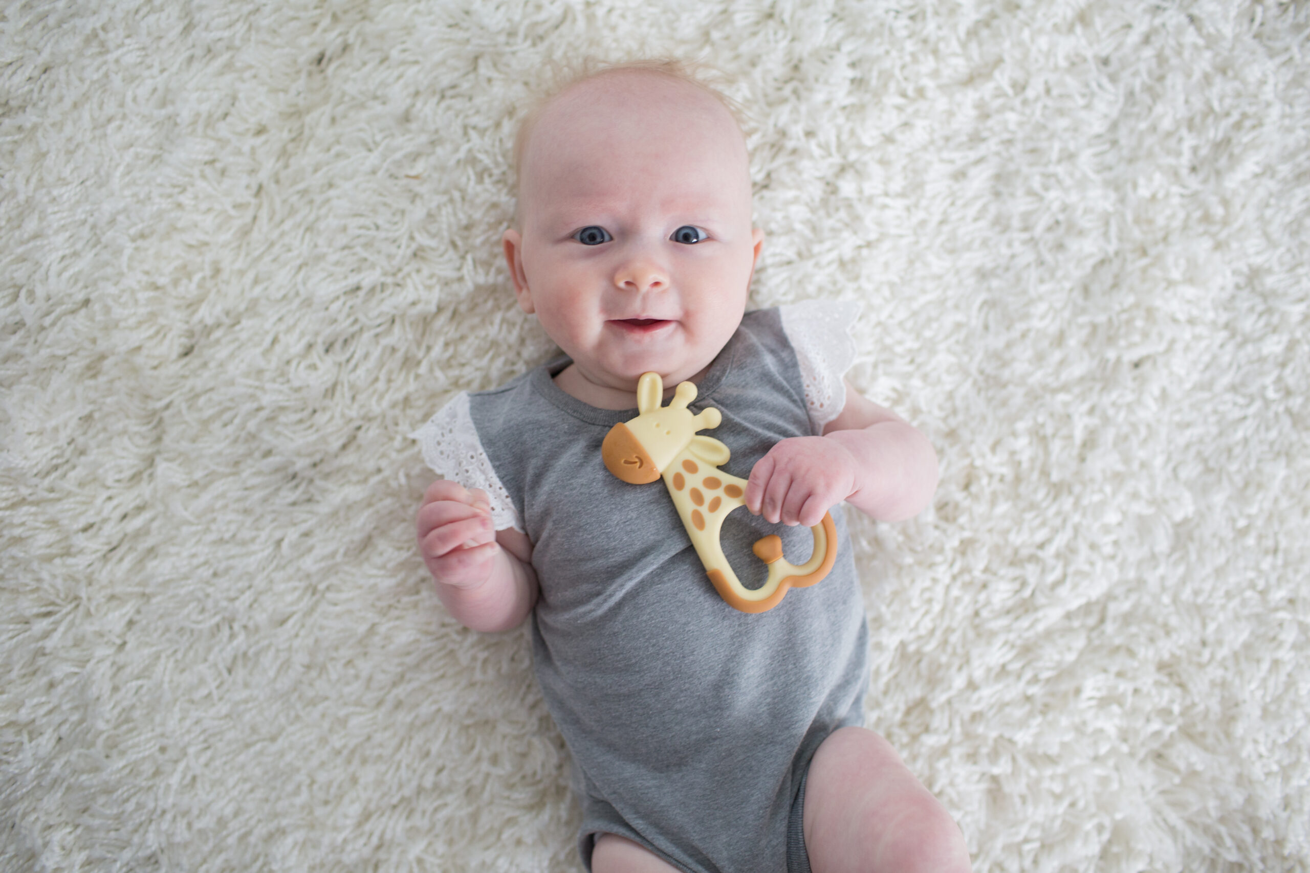 Happy Kids Boutique afbeelding van een baby die op een zachte ondergrond ligt en een bijtring vasthoudt, geschikt bij doorkomende tandjes, waarbij de baby rustig speelt met een Dr. Brown's bijtring