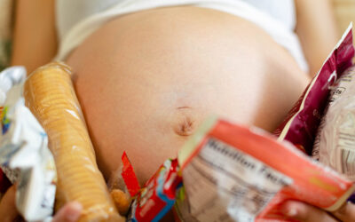 Happy Kids Boutique zwanger zwangerschapscravings met close up van een zwangere buik omringd door verschillende snacks zoals koekjes en verpakte lekkernijen die trek tijdens de zwangerschap laten zien