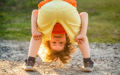 Happy Kids Boutique ondeugend kind dat buiten speelt en ondersteboven door zijn benen kijkt op een zonnig pad, speels en vrolijk moment in de natuur