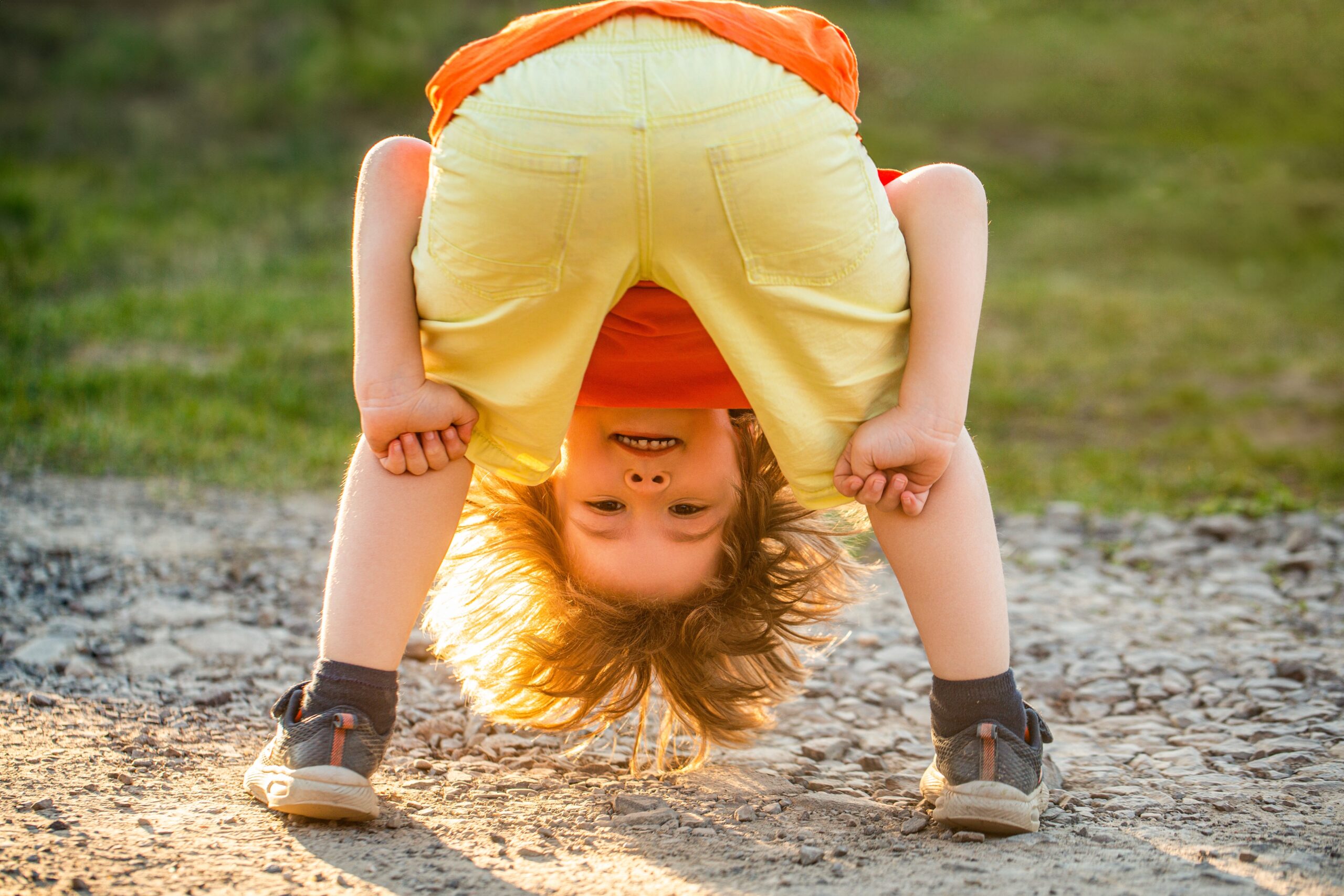 Happy Kids Boutique ondeugend kind dat buiten speelt en ondersteboven door zijn benen kijkt op een zonnig pad, speels en vrolijk moment in de natuur