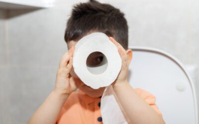 Blogfoto zindelijkheid overdag Happy Kids Boutique kind houdt wc-papier voor zijn gezicht tijdens het oefenen op de wc, speelse lifestyle afbeelding over zindelijkheid en zindelijk worden bij jonge kinderen