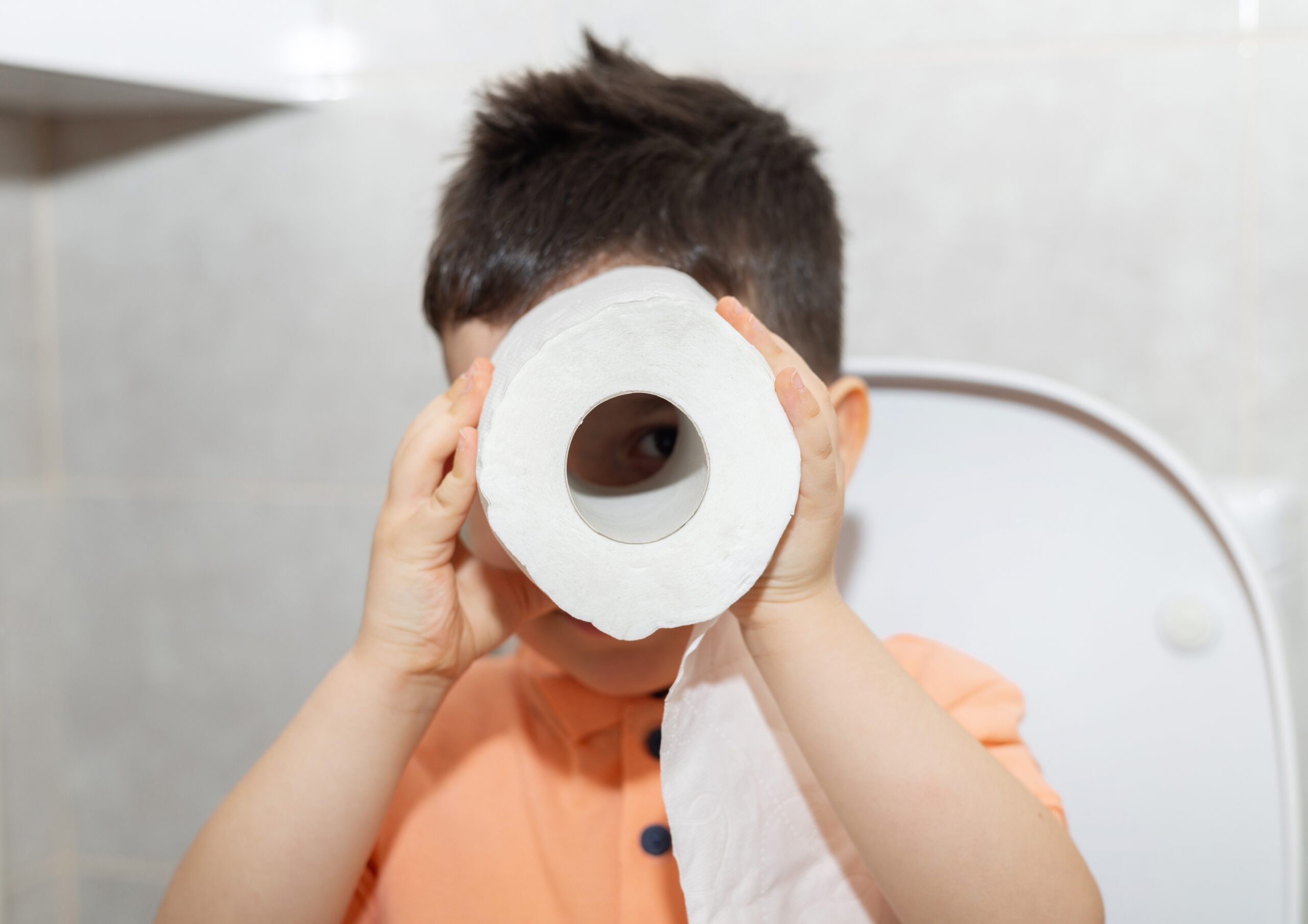 Happy Kids Boutique kind houdt wc-papier voor zijn gezicht tijdens het oefenen op de wc, speelse lifestyle afbeelding over zindelijkheid en zindelijk worden bij jonge kinderen