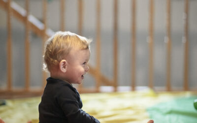 Happy Kids Boutique kind zit lachend te spelen op een kleurrijke mat, vrolijke lifestyle afbeelding over kinderen, binnenactiviteiten en indoor spelen op een rustige speelplek.