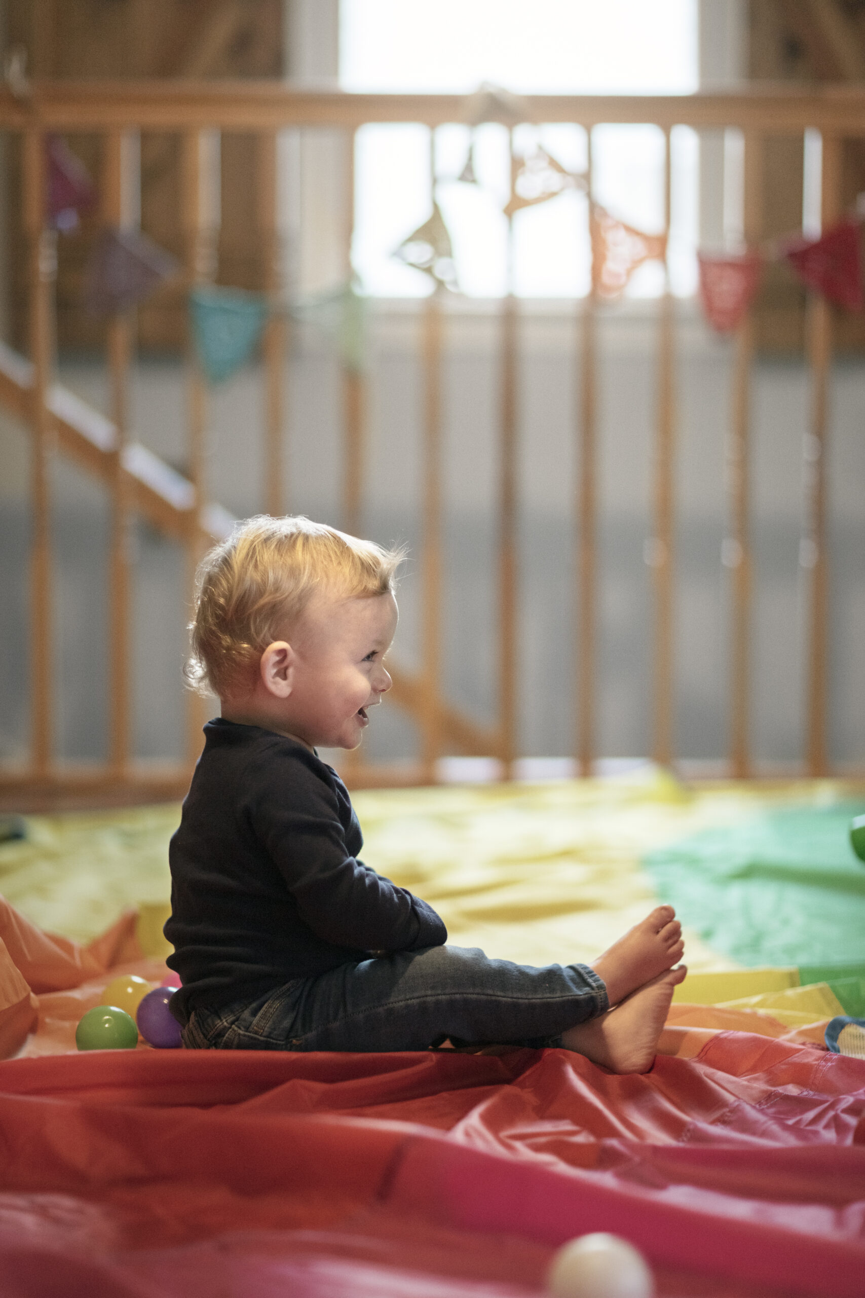 Happy Kids Boutique kind zit lachend te spelen op een kleurrijke mat, vrolijke lifestyle afbeelding over kinderen, binnenactiviteiten en indoor spelen op een rustige speelplek.