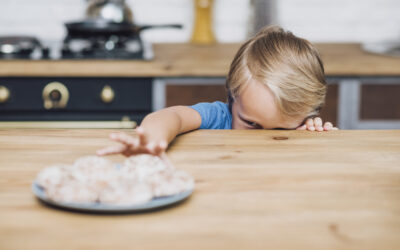 Happy Kids Boutique kind reikt naar eten op tafel en duwt bord weg, herkenbare lifestyle afbeelding over een moeilijke eter en eetmomenten met jonge kinderen.