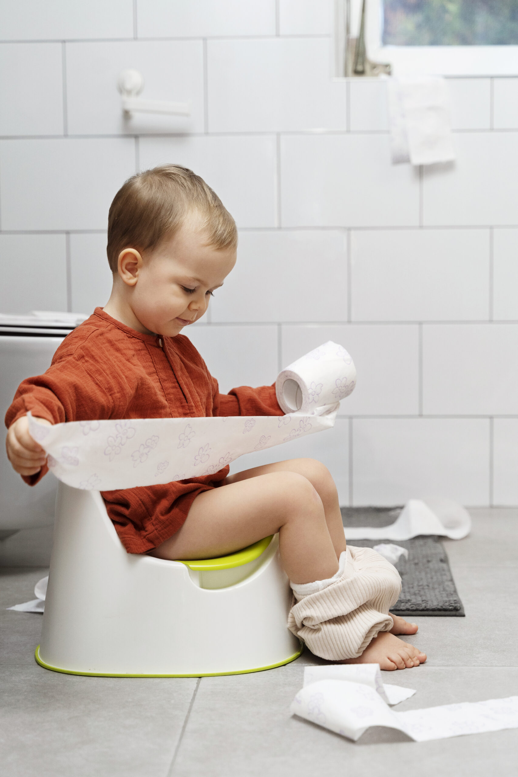 Happy Kids Boutique kind zit op een potje in de badkamer en rolt toiletpapier af tijdens het oefenen van zindelijkheid, speelse en herkenbare situatie met aandacht voor zelfstandigheid en duurzaamheid
