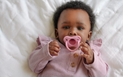 Happy Kids Boutique baby met roze Dr. Brown's fopspeen liggend op een wit dekentje, kindje draagt roze kleding en kijkt rustig naar de camera, lifestyle afbeelding van een comfortabele fopspeen voor dagelijks gebruik