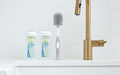 Happy Kids Boutique babyfles reinigen en schoonmaken met flessenborstel naast de gootsteen, twee Dr. Brown’s babyflessen en grijze borstel op het aanrecht, lifestyle afbeelding over hygiëne en dagelijkse verzorging.