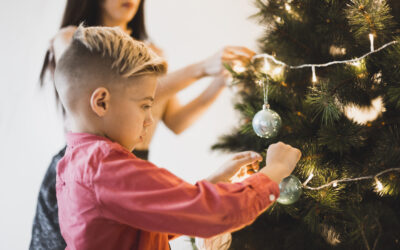 Blogfoto kerst en geloof Happy Kids Boutique kind versiert samen met volwassene de kerstboom met lichtjes en kerstballen, warme lifestyle afbeelding over kerst, geloof en samen momenten beleven tijdens de feestdagen