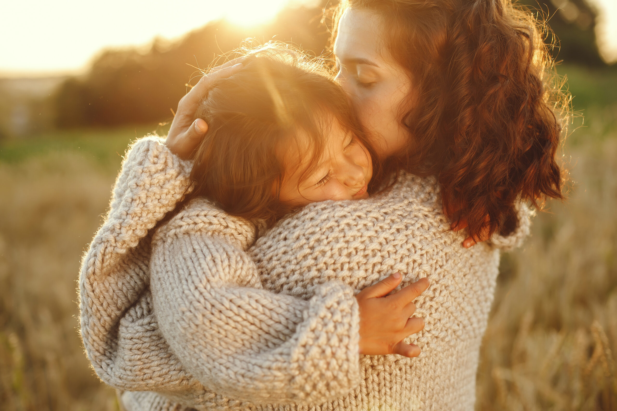Happy Kids Boutique moeder en kind omhelzen elkaar in een warm verlicht veld, liefdevol moment dat gevoelens, emoties en interactie tussen ouder en kind laat zien