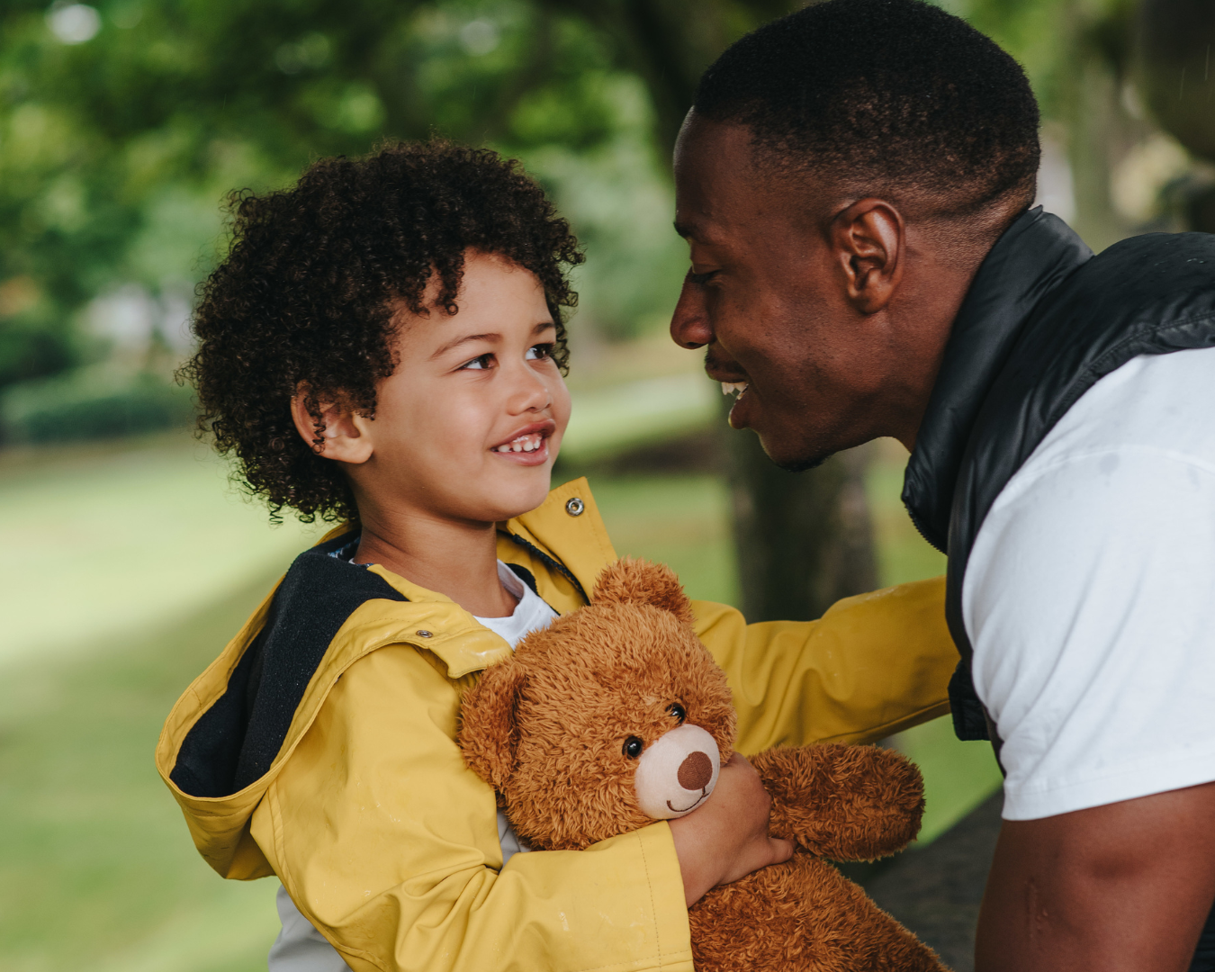 vader en kind kijken elkaar lachend aan. Kind houd een teddybeer vast