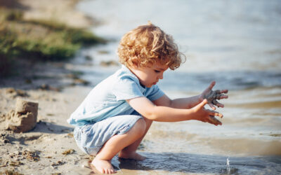 Kind speelt op het strand met zand en water, passend bij Happy Kids Boutique, vrij spel, ontdekken en strandactiviteiten voor kinderen.