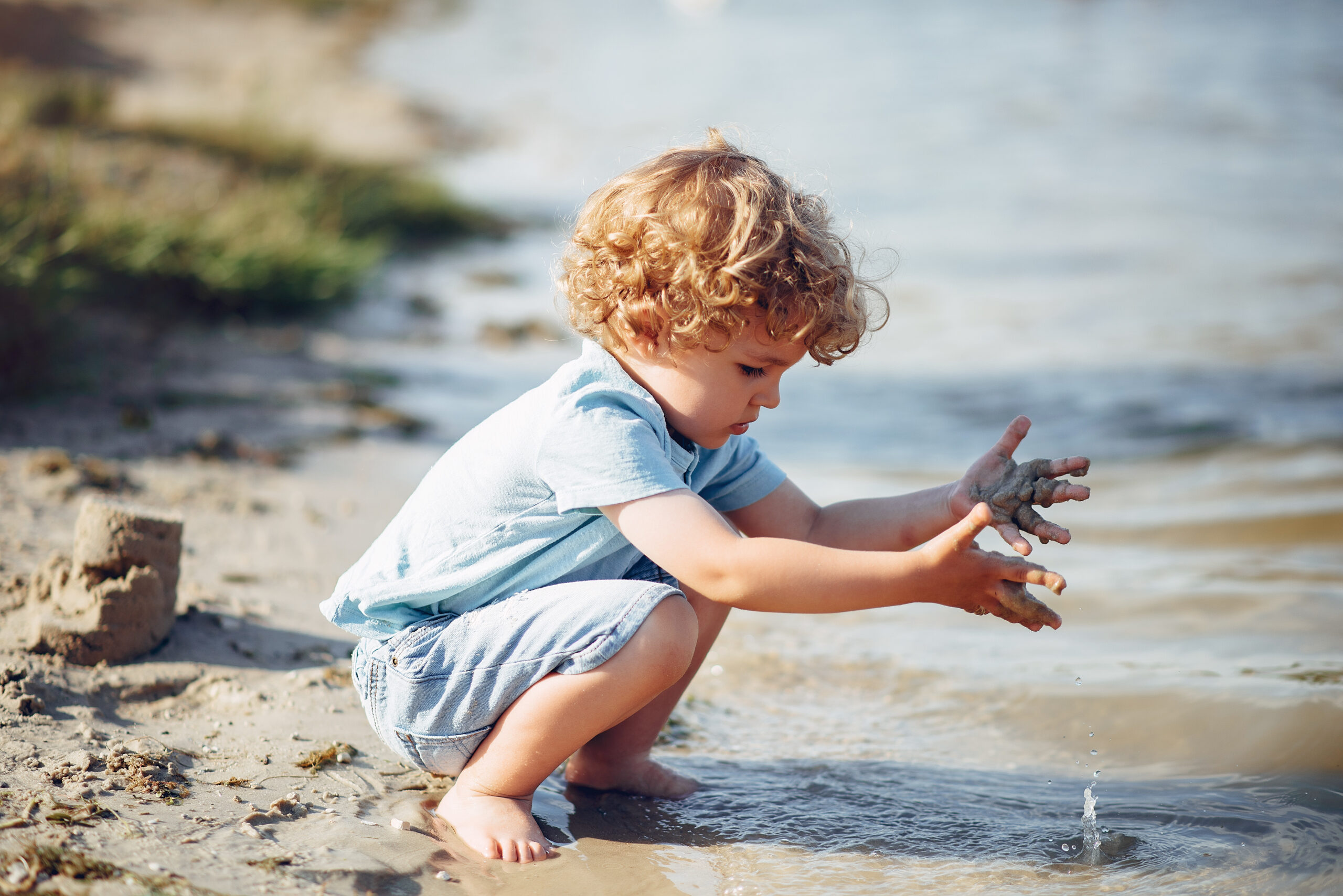 Kind speelt op het strand met zand en water, passend bij Happy Kids Boutique, vrij spel, ontdekken en strandactiviteiten voor kinderen.
