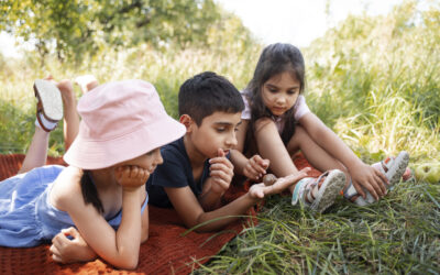 Happy Kids Boutique kinderen liggen samen op een kleed in de natuur en bekijken een slak, vrolijke lifestyle afbeelding over vakantie, nieuwe ontdekkingen en kennismaken met de wereld.