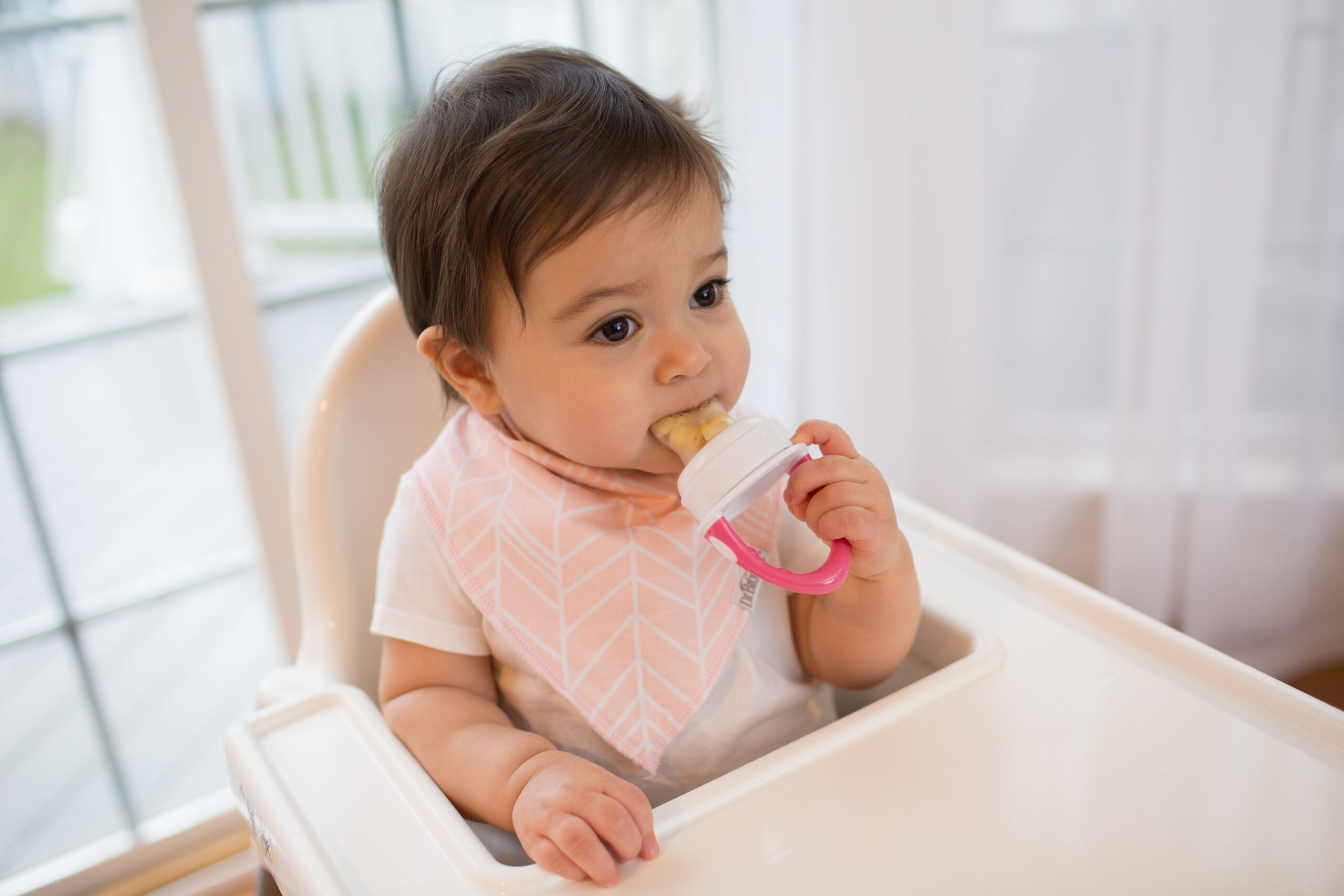 Happy Kids Boutique baby zit in kinderstoel en gebruikt de Dr. Brown's silicone feeder met fruit, lifestyle afbeelding over smaakontwikkeling en het ontdekken van eerste hapjes op een veilige en rustige manier.