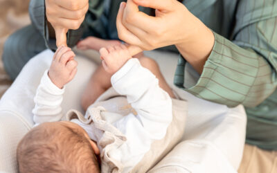 Happy Kids Boutique baby ligt op schoot en raakt de vingers van een ouder aan, liefdevolle lifestyle afbeelding over babygebaren en communiceren met je kindje.