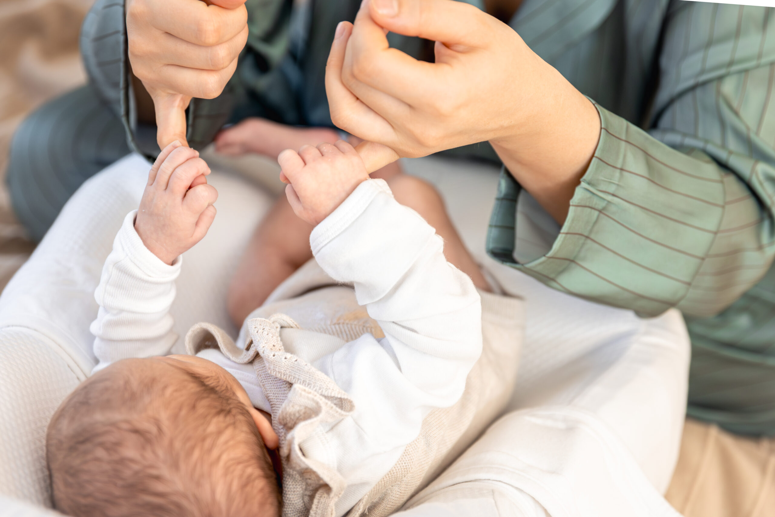 Happy Kids Boutique baby ligt op schoot en raakt de vingers van een ouder aan, liefdevolle lifestyle afbeelding over babygebaren en communiceren met je kindje.