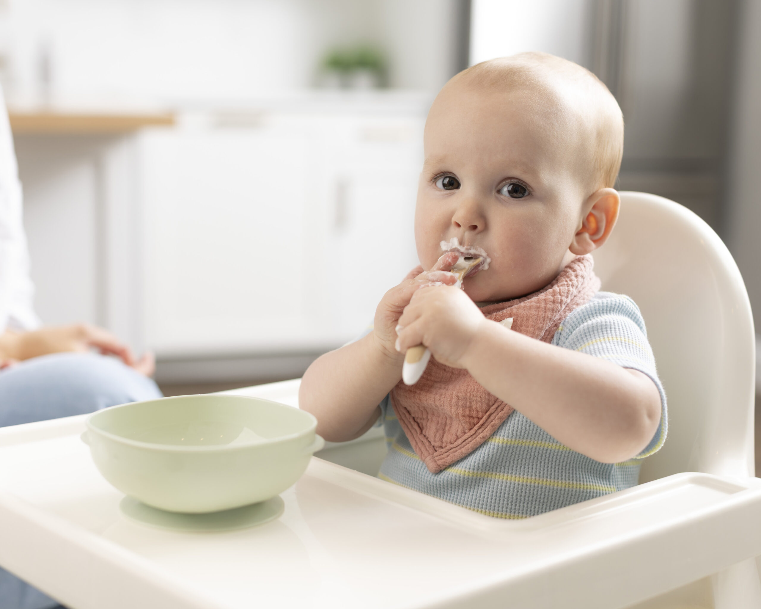 Baby in een kinderstoel eet zelfstandig de eerste vaste voeding met een lepeltje.