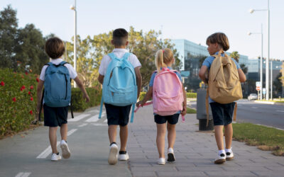 Vier kinderen met rugzakken lopen samen naar school na de zomervakantie.