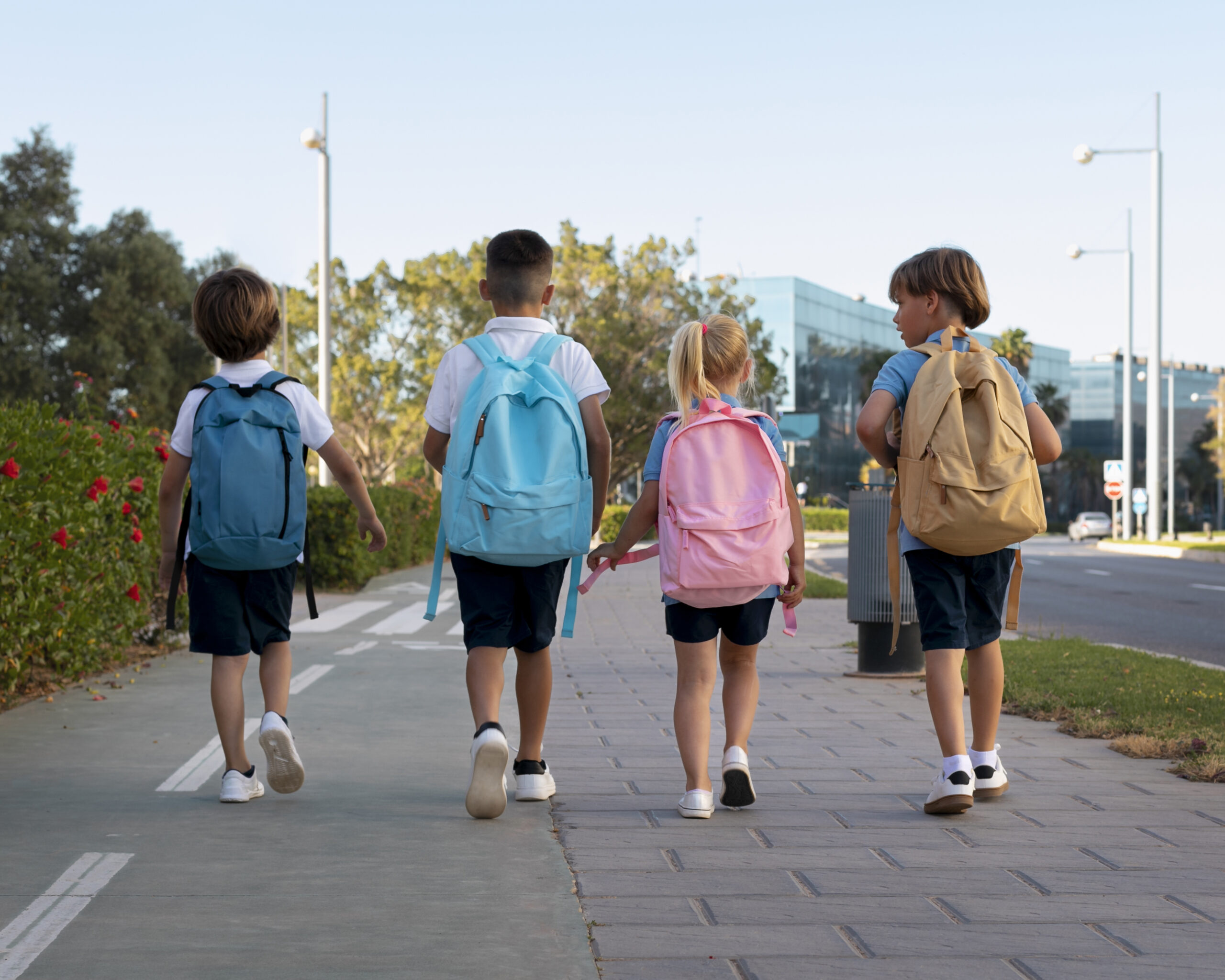 Vier kinderen met rugzakken lopen samen naar school na de zomervakantie.