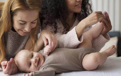 Twee moeders verzorgen samen een lachende baby tijdens een rustig verzorgingsmoment thuis.