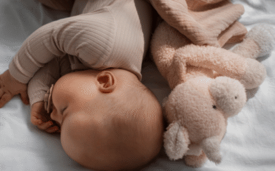Slapende baby ligt knus naast een zacht knuffeltje in bed.