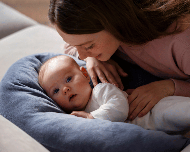 Moeder ligt liefdevol naast haar baby op een voedingskussen tijdens een rustig moment samen.