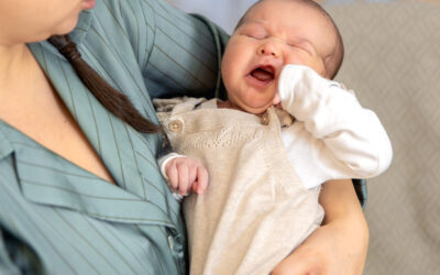 Gapende baby ligt ontspannen in de armen van een ouder en draagt een zacht beige pakje.