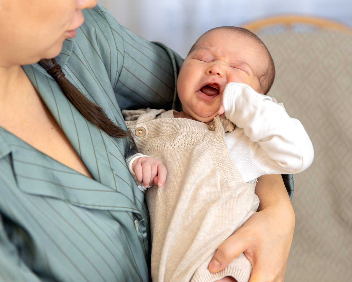 a mother holds a newborn baby in her arms. newborn baby. Gapende baby ligt ontspannen in de armen van een ouder en draagt een zacht beige pakje.