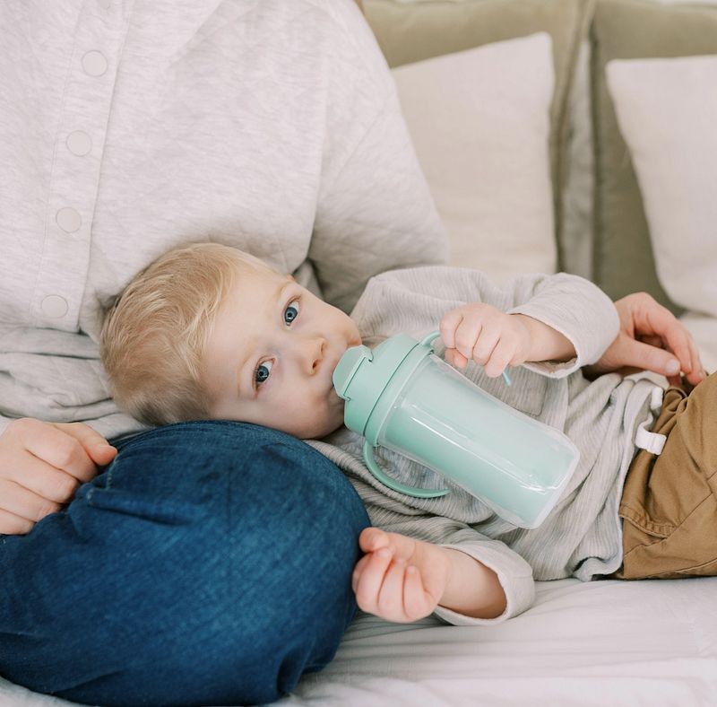 Kindje drinkt uit de lichtgroene Dr. Brown's geïsoleerde rietjesbeker van 300 ml met handvatten