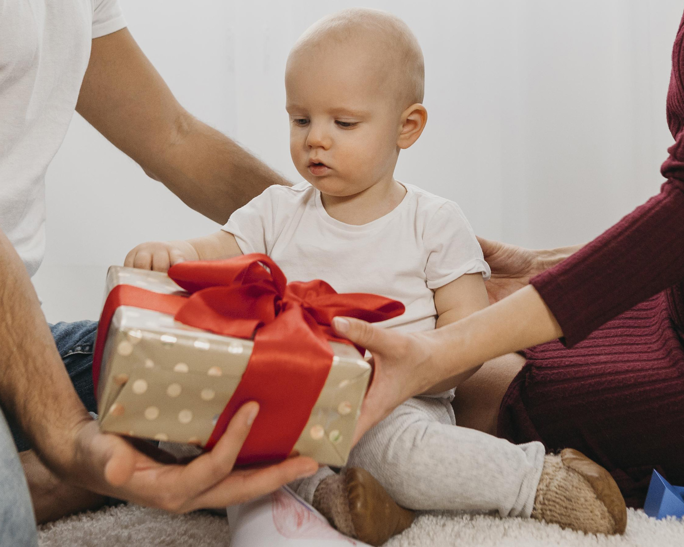 Baby krijgt van zijn ouders een ingepakt cadeautje met een grote rode strik voor Sinterklaas.