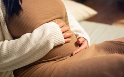 Zwangere vrouw zit ontspannen op de bank en houdt haar handen liefdevol op haar babybuik tijdens de voorbereiding op de komst van haar kleintje.