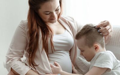 Zwangere moeder zit samen met haar zoontje op de bank, terwijl hij liefdevol haar babybuik aanraakt in afwachting van zijn broertje of zusje.